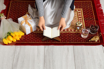 Young Muslim woman with Koran on praying mat, closeup. Ramadan celebration