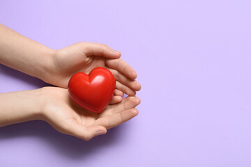 Obraz premium Female hands with red heart on lilac background
