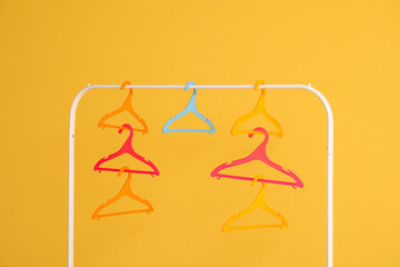 Rack with plastic clothes hangers on yellow background
