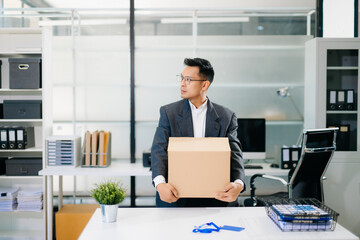Sad businessman sitting in office with box and ID card after layoff, feeling exhausted and depressed from job loss and workplace stress.