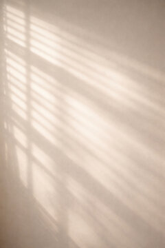 Warm sunlight casting abstract shadows of window blinds on a light beige wall, creating a serene and minimalist aesthetic.