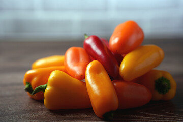 a vibrant cluster of colorful mini bell peppers in shades of orange, yellow, and red placed on a wooden surface against a softly blurred neutral background, highlighting their glossy texture and fresh