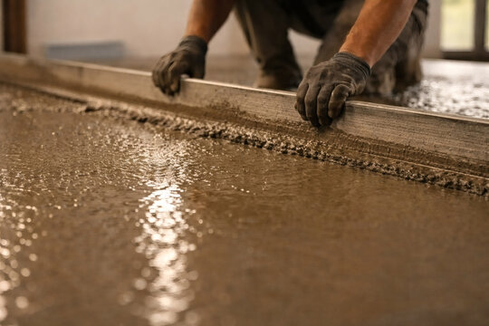 Smoothing fresh concrete: A construction worker uses a straight edge to level out and perfect a newly poured concrete floor with precision.
