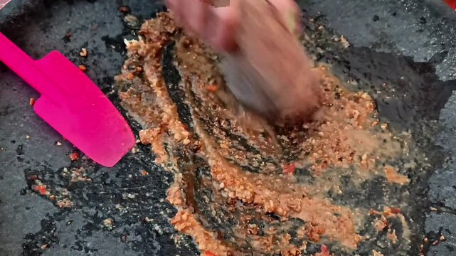 A woman grinds peanuts and spices with a pestle, preparing the base for Rujak Cingur.