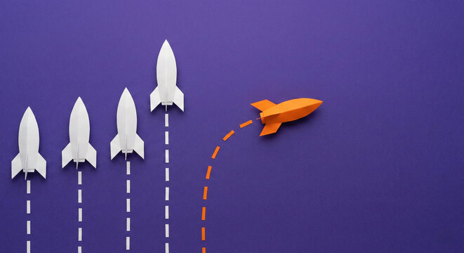 Orange rocket changing direction from white rockets with dashed trails, concept of startup strategy