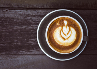 Top view of hot coffee latte art in a ceramic cup on dark wooden background with copy space.