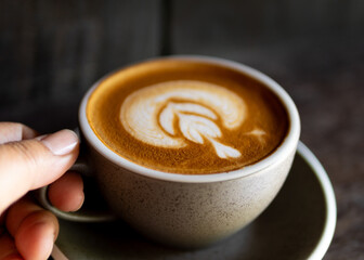 Close up of hand holding a cup of hot coffee latte with beautiful latte art on wooden table
