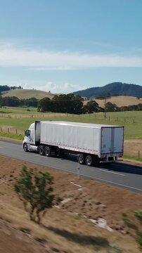 Large freight truck driving on a scenic highway with green fields and mountains, vertical shot