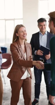 Businesswoman greeting company client with handshake during group meeting in office, represent successful negotiations result, closing business deal, congratulate each other with partnership starting