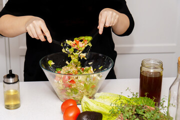 Person preparing a fresh vegetable salad in a glass bowl, promoting healthy eating and cooking at home