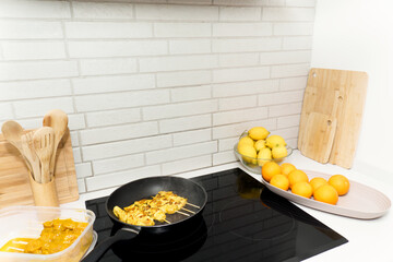 Marinated chicken skewers frying in a pan on a modern induction hob with fresh fruit and kitchen utensils nearby