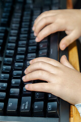 Young child hands pressing keys on a black computer keyboard, learning and interacting with modern digital technology