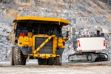 Fototapeta premium Massive Mining Machinery in Quarry: Yellow Dump Truck and Excavator at Work