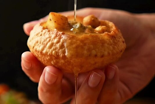 cinematic view of hand holding pani puri where mint water is poured
