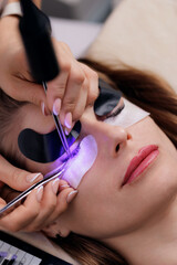 Female receiving eyelash led extensions procedure with UV light therapy