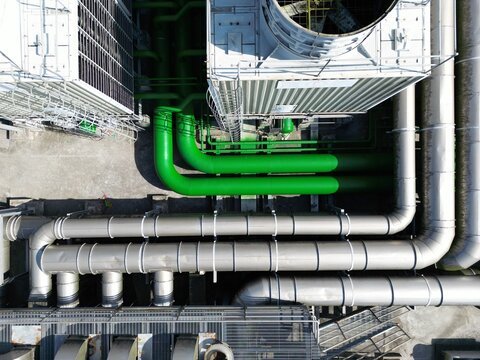 Top down aerial view of green and silver industrial pipelines connecting to cooling towers for AI data center.