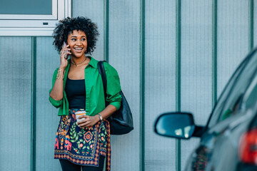 young woman with afro hair talking on the phone at street wall with cars, copy-space
