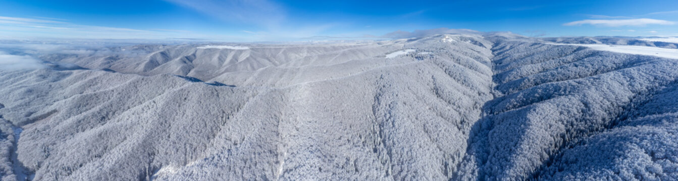 Panoramic view of a snow-covered mountain landscape under a clear blue sky,taken from a drone. Aerial view of the Gurghiu mountains in the Sovata resort area covered in snow in winter