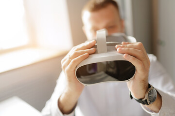 Caucasian male adult hold virtual reality VR headset in sunlight room, immersive technology concept