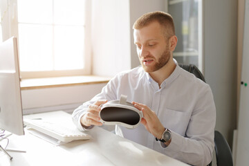 Young caucasian male examining vr headset in bright office setting, futuristic and innovative workplace for data analysis