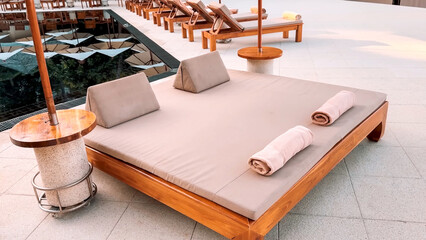 Luxury double sunbed with pillows and towels next to a reflective swimming pool