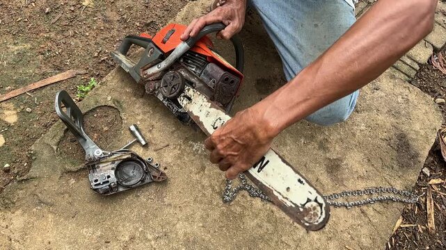 A skilled local mechanic performing maintenance and fixing a gasoline chainsaw engine in a rustic rural setting surrounded by tools.