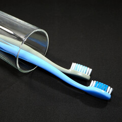 A pair of toothbrushes in a clear glass on black background closeup shot, conveying a sense of oral hygiene and daily routine with a touch of vibrancy.