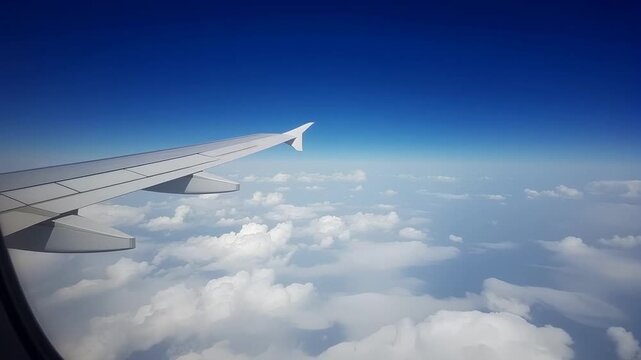 Modern airplane wing with white winglet flying over white fluffy clouds in bright daylight, clear blue sky aerial view, commercial aviation transport and tourism business travel concept.