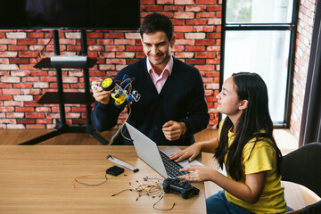 A curious girl student and supportive male teacher explore coding and electronics on a laptop in a modern classroom, capturing hands-on learning, STEM discovery, and joyful tech education for kids.