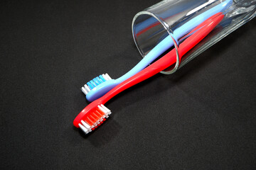 A pair of colorful toothbrushes in a clear glass on black background closeup shot, conveying a sense of oral hygiene and daily routine with a touch of vibrancy.