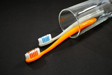 A set of colorful toothbrushes in a clear glass on black background closeup shot, conveying a sense of oral hygiene and daily routine with a touch of vibrancy.