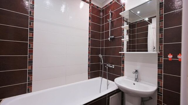 Compact bathroom with dark brown tiled walls, white bathtub, pedestal sink, mirror cabinet, shower head, clean and functional layout.
