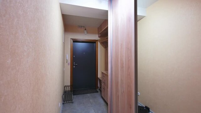 narrow hallway with wooden sliding doors, built-in shelving, dark door at the end, robotic vacuum cleaner on the floor, neutral-toned walls, recessed ceiling lights. Compact, functional space.