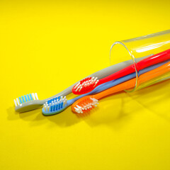 Colorful toothbrushes in a clear glass red, orange, blue, and grey on a sleek yellow background, evoking a sense of cleanliness and oral health, Daily routine concept photography