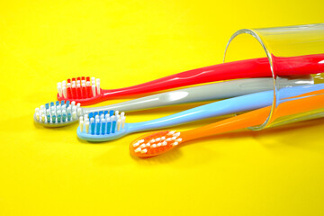 Colorful toothbrushes in a clear glass red, orange, blue, and grey on a sleek yellow background, evoking a sense of cleanliness and oral health, Daily routine concept photography