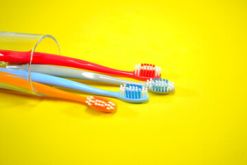 Vibrant toothbrushes in a clear glass red, orange, blue, and grey on a sleek yellow background, evoking a sense of cleanliness and oral health, Daily routine concept photography