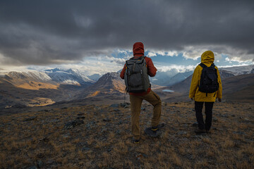 Hikers in bright clothing have stopped on a mountain road to admire a stunning valley during golden...