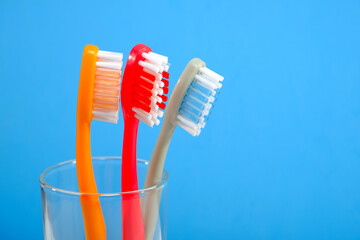 Vibrant toothbrushes in red, orange, and grey in clear glass on blue background with copy space, evoking a sense of cleanliness and oral health, Daily routine concept photography