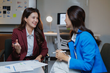 Two businesswomen are engaging in a focused discussion, sharing insights and actively collaborating on a project plan with documents and charts on the table in an office setting