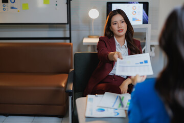 Professional businesswoman in a suit discussing data, presenting a document with charts and graphs to a colleague during a corporate business meeting in a modern office