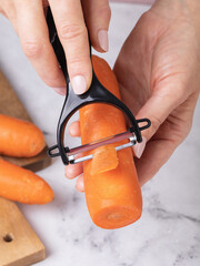 A woman peeling a carrot with a vegetable peeler on a table, close-up, authentic photograph, not AI-generated.