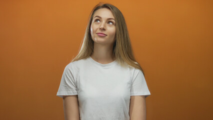 Woman smiling thoughtfully in a white shirt against an orange background, conveying a positive and isolated mood with a youthful vibe.