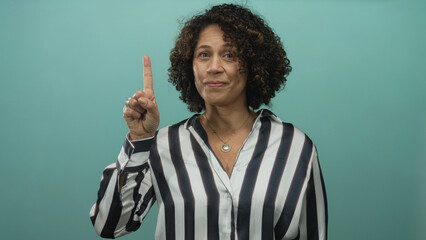 Woman in a striped shirt holds up index finger adorned with a silver ring in a teal studio set;...
