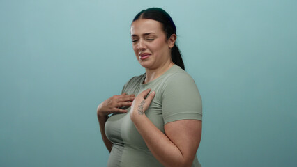 Obraz premium Woman displaying a gesture of disgust against a blue background, wearing a light green shirt, exemplifying negative emotion and body language in a simple studio setup.