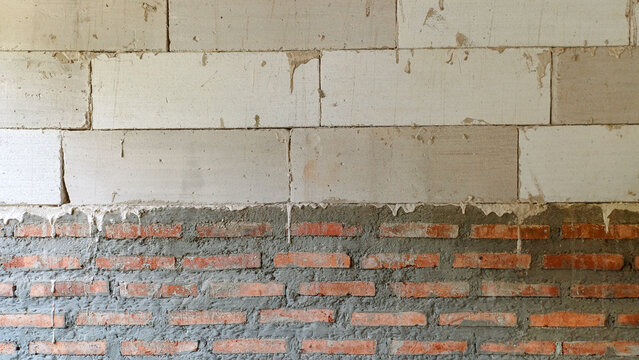 Wall construction showing transition between white lightweight blocks and red clay bricks. Raw industrial texture for building, masonry, and architectural design.