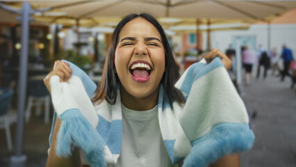 Woman lifts scarf while cheering at a restaurant with young latin hispanic friends on a terrace during an outdoor sports celebration. © Krakenimages.com