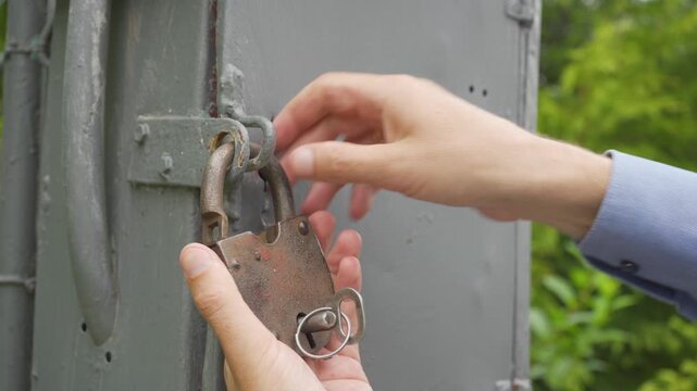 Inserting a key into a rusty padlock, A man opens an old lock with a key