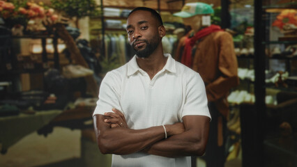Obraz premium Man with arms crossed wearing a white polo shirt in building retail display; thoughtful reflection pause.