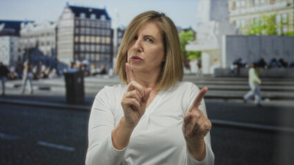 Caucasian middle aged woman pointing index finger to reject on urban street with blurred bystanders; defiance.