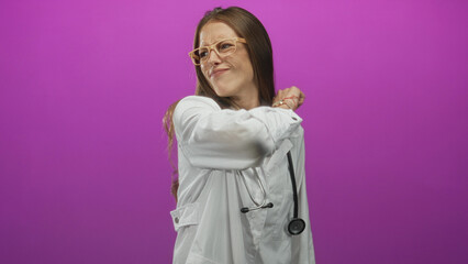Woman doctor wearing white coat and stethoscope pointing her arm outward to the right in magenta studio; urgency readiness.